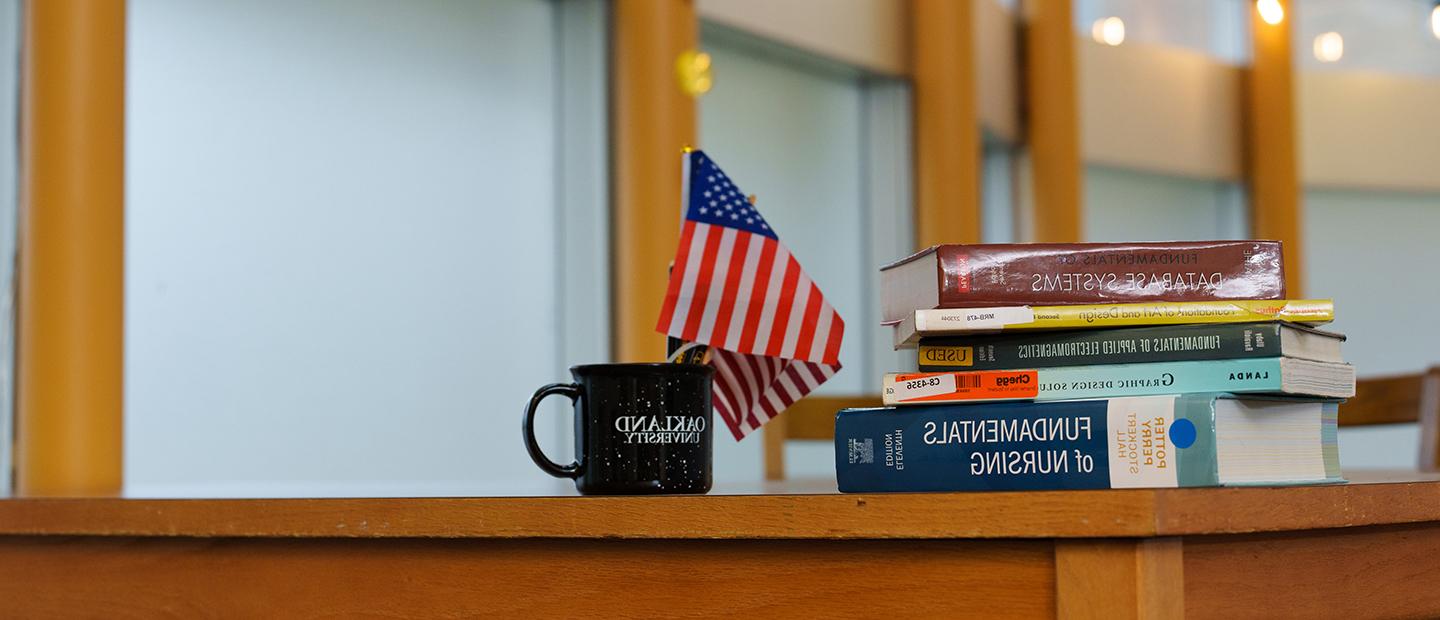 桌子上放着一堆教科书，旁边还有一个韦德体育app官网的咖啡杯，里面有几面小美国国旗.